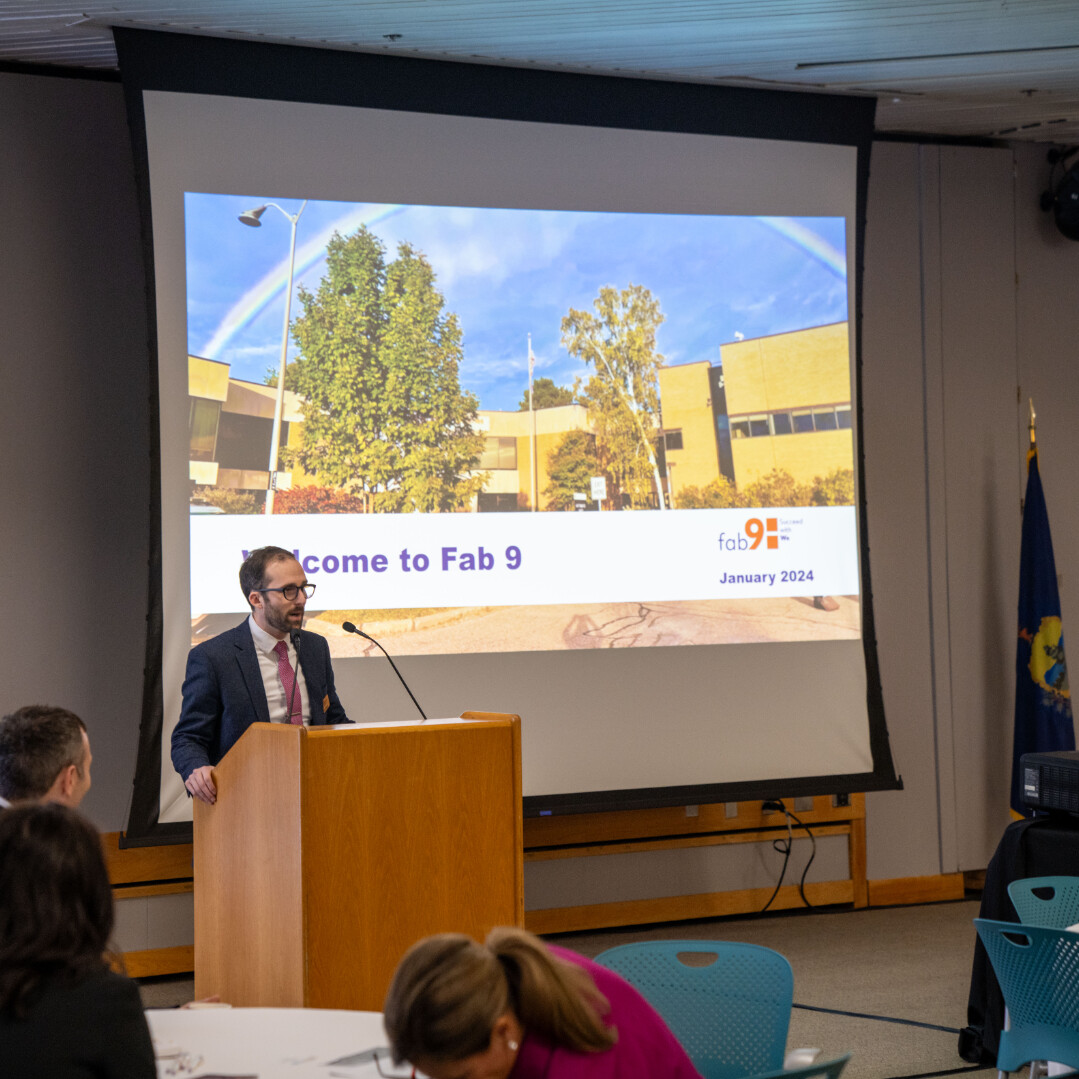 Speaker at a podium in front of a presentation titled "Welcome to Fab 9, January 2024."