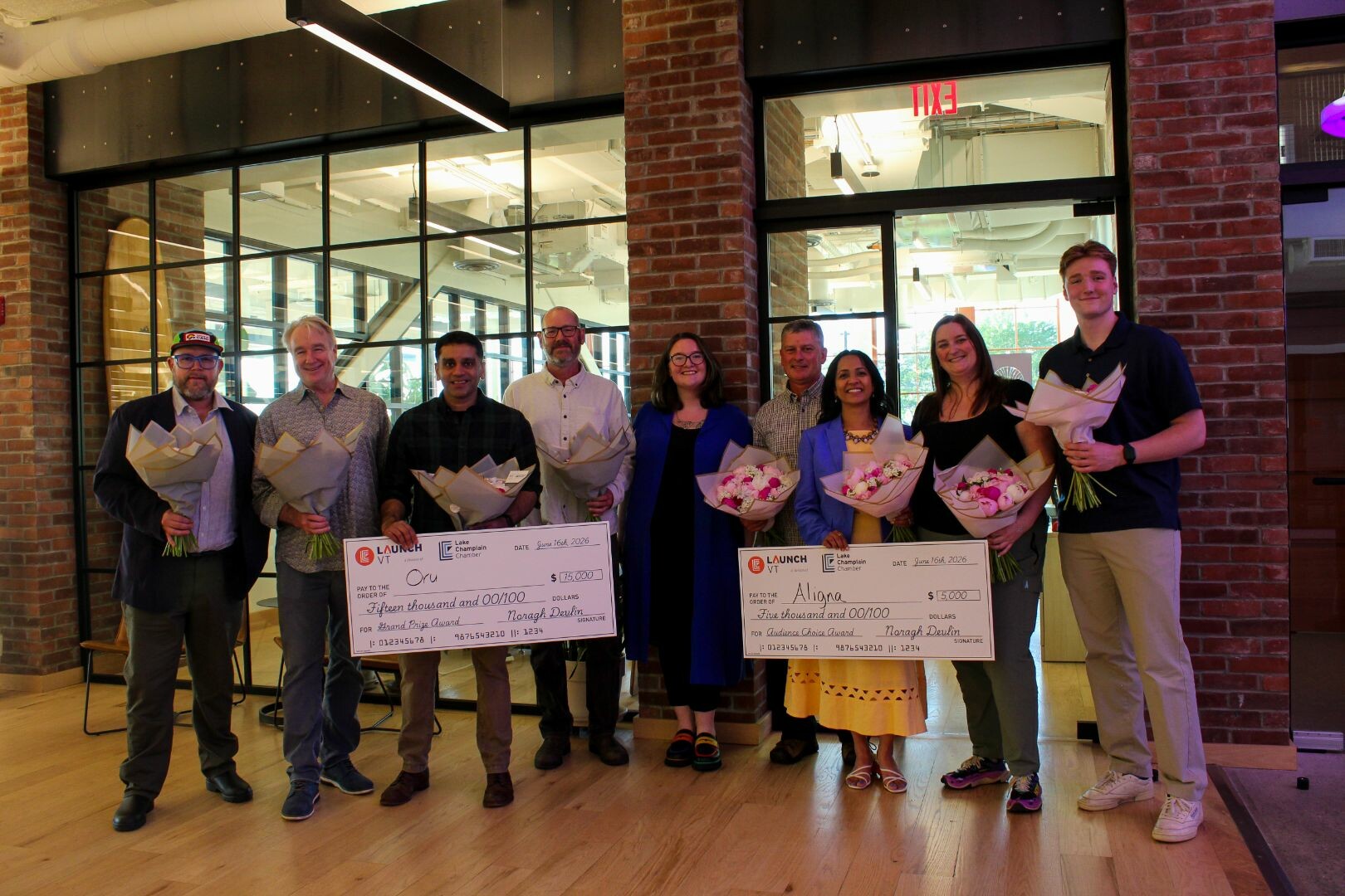 Group photo of award recipients holding checks and flowers at a ceremony.