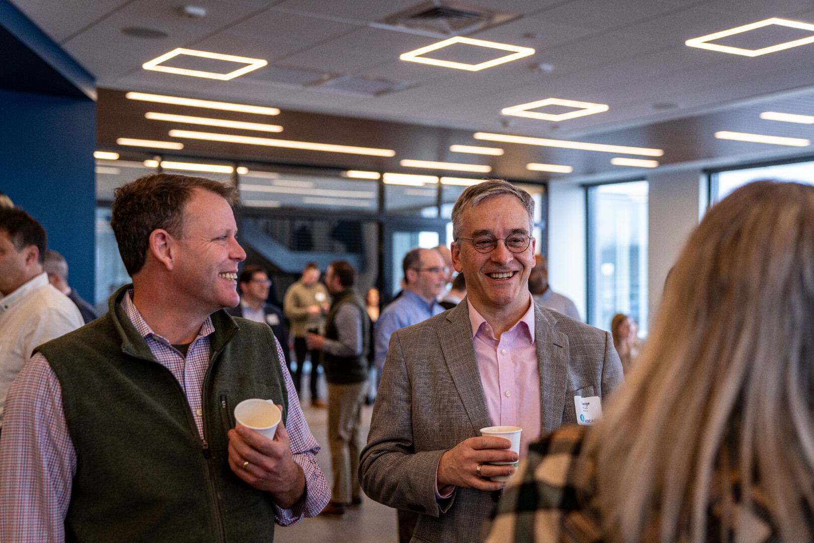 Two men smiling and chatting at a networking event, cups in hand.