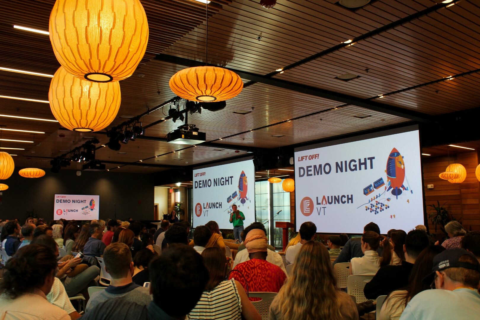 Audience at a "Demo Night" event with presentations and vibrant hanging lanterns.