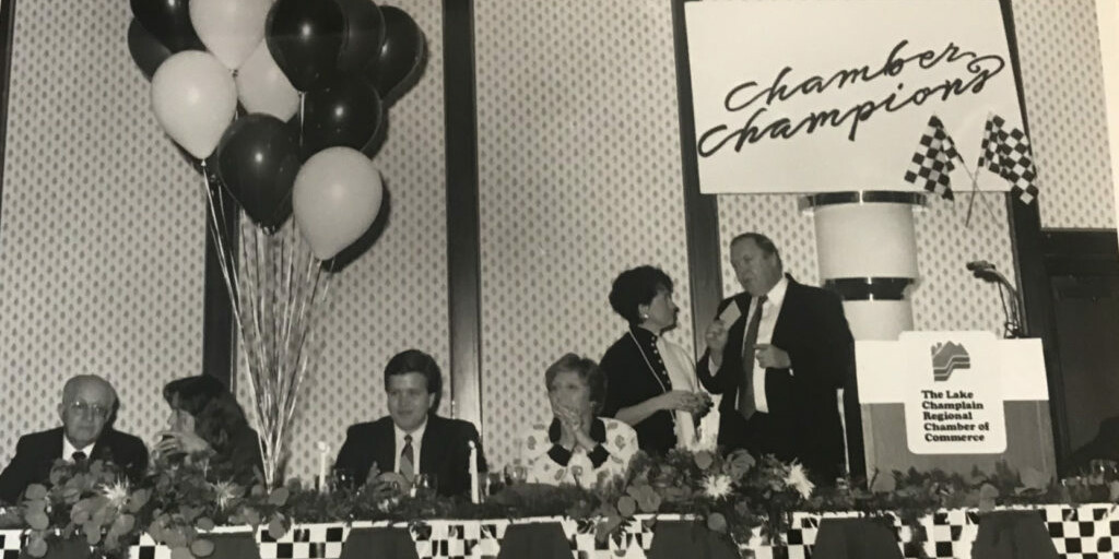 Panel discussion at a Chamber of Commerce event with balloons and a "Chamber Champions" sign.