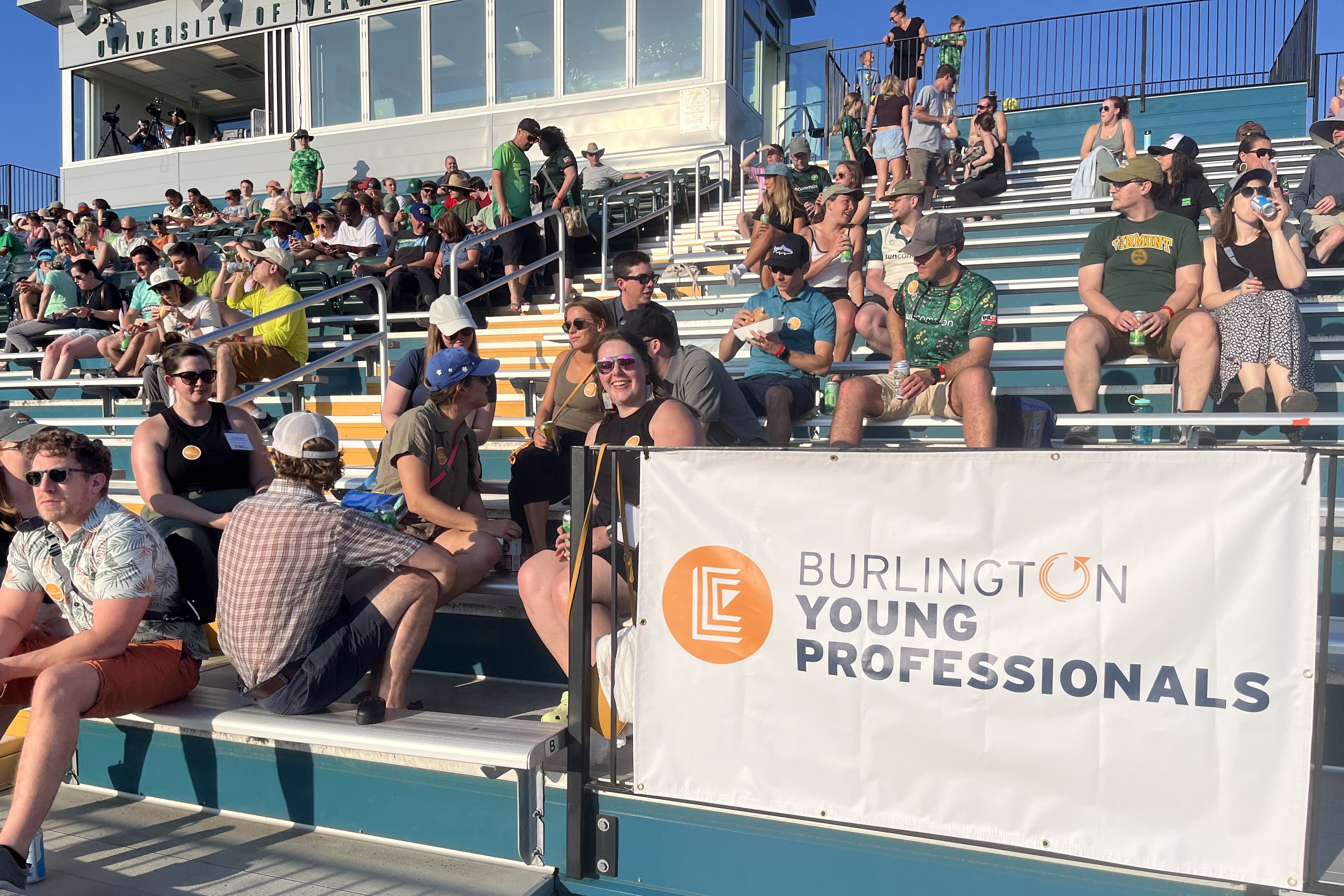 Crowd of people sitting in bleachers, with a banner for Burlington Young Professionals.