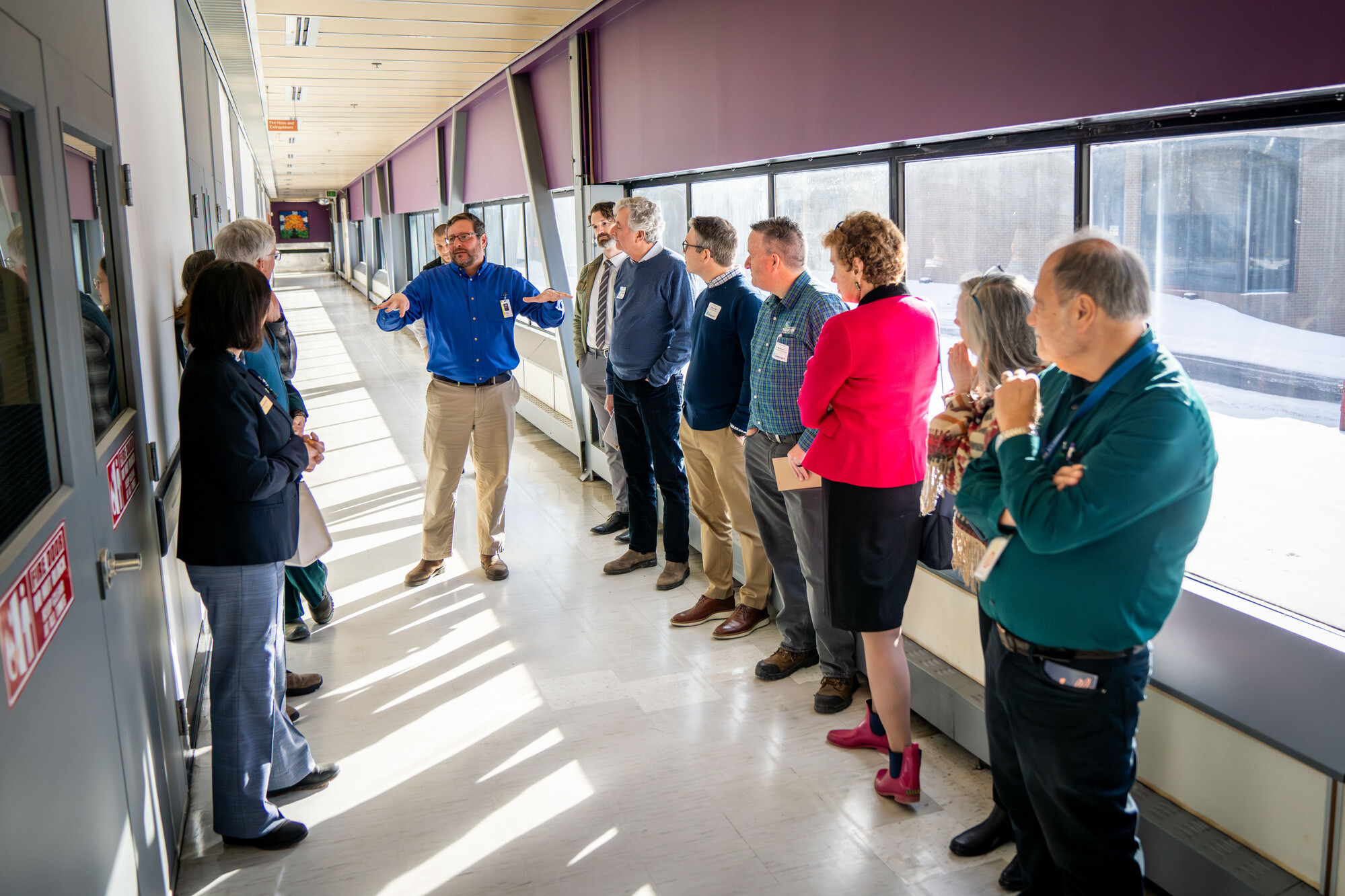 A group of people listening to a speaker in a brightly lit corridor.