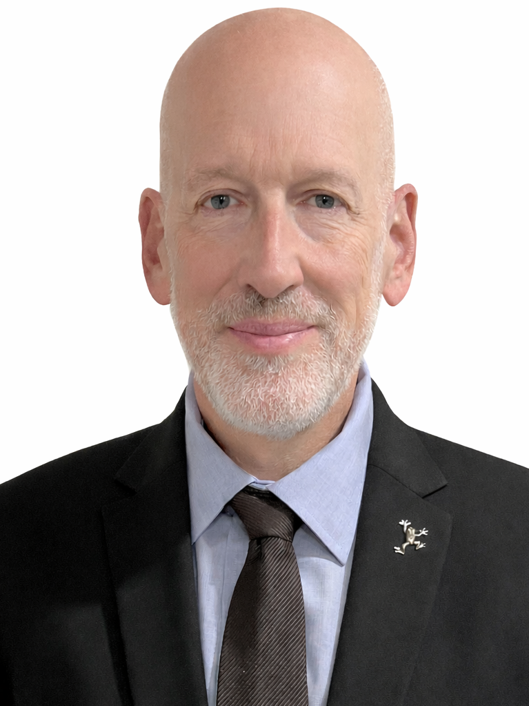A smiling bald man in a suit with a tie, wearing a decorative lapel pin.