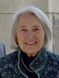 Smiling older woman with gray hair, wearing a patterned jacket and pearls.