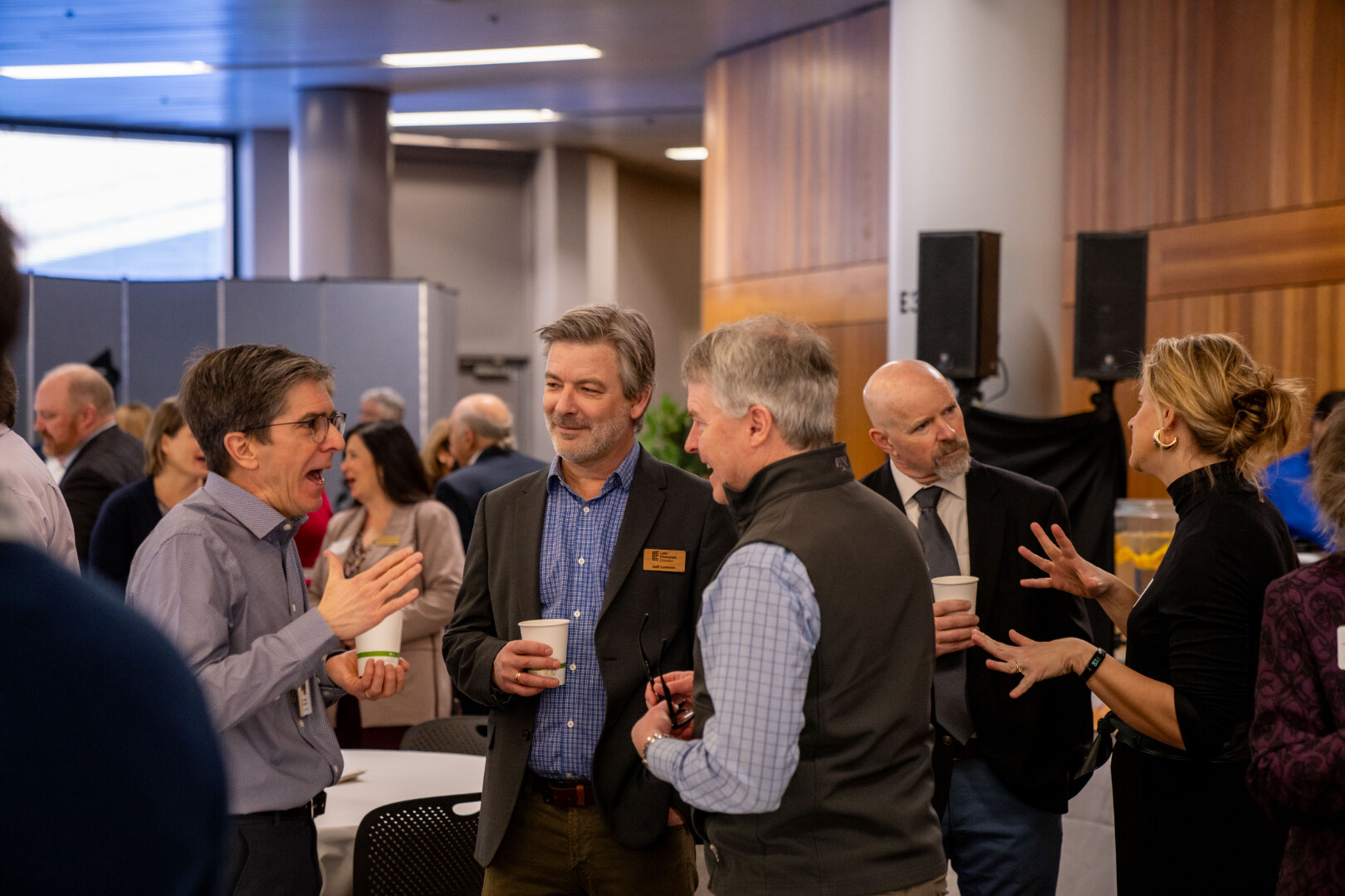 Group of people networking and chatting at a conference, holding cups in a modern venue.