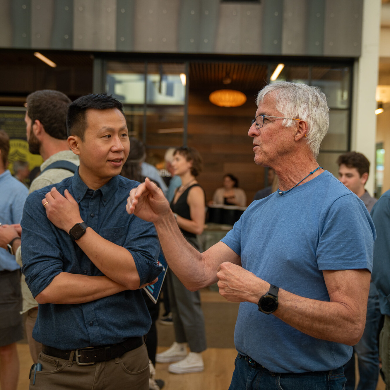 Two men engaged in conversation at a lively indoor gathering.