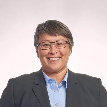 Smiling person in a dark suit and glasses, set against a light background.