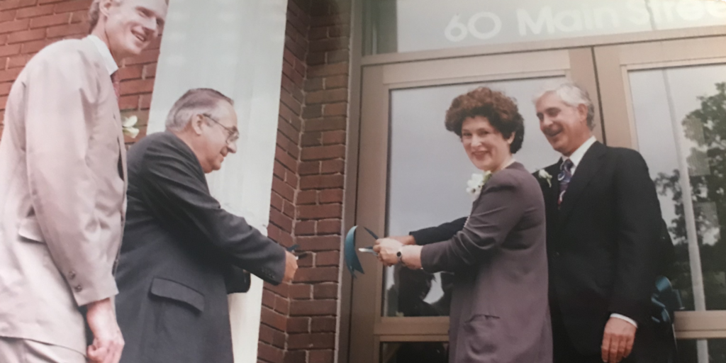 A woman cuts a ribbon at a building opening, flanked by three men.