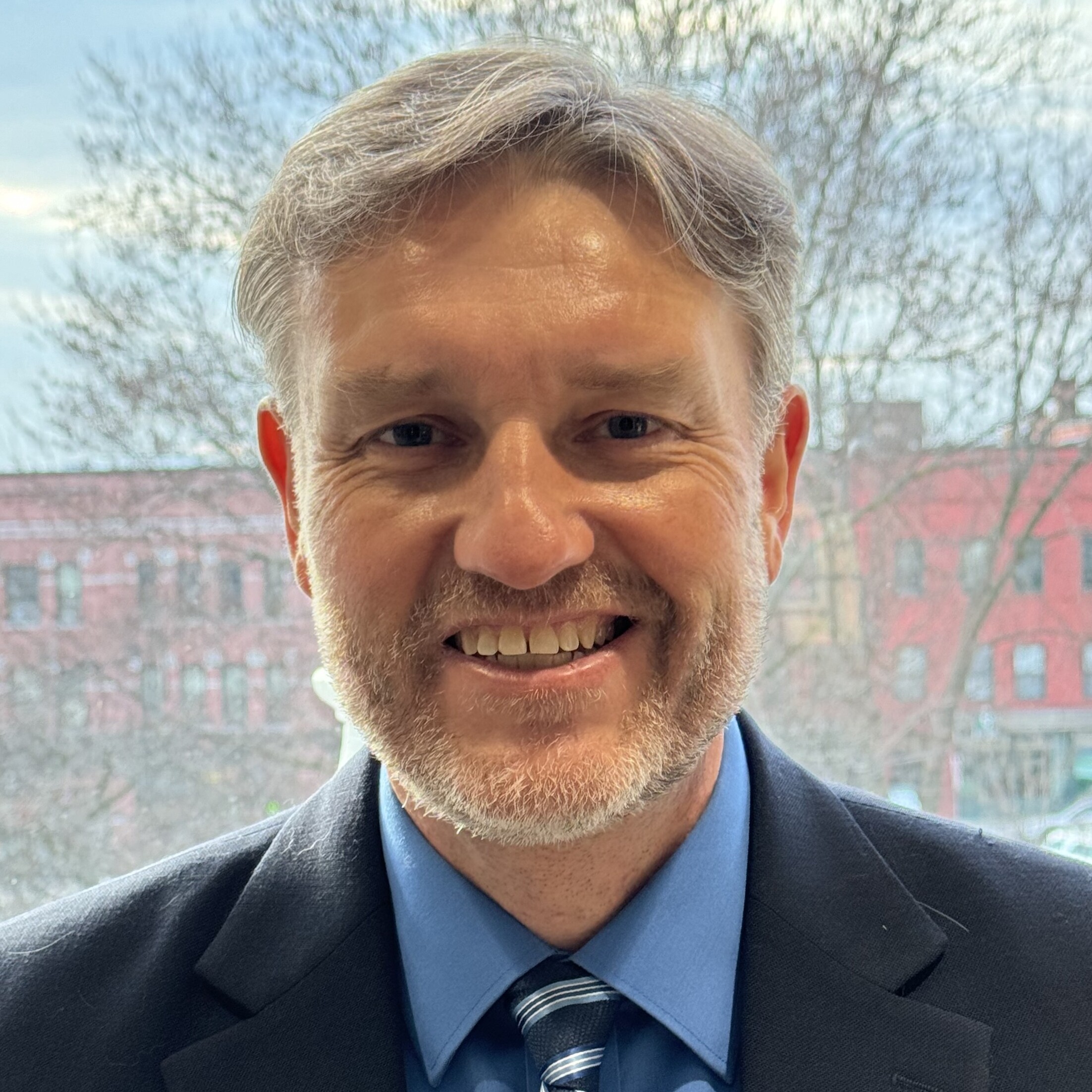 A smiling man in a suit and tie with a city backdrop.