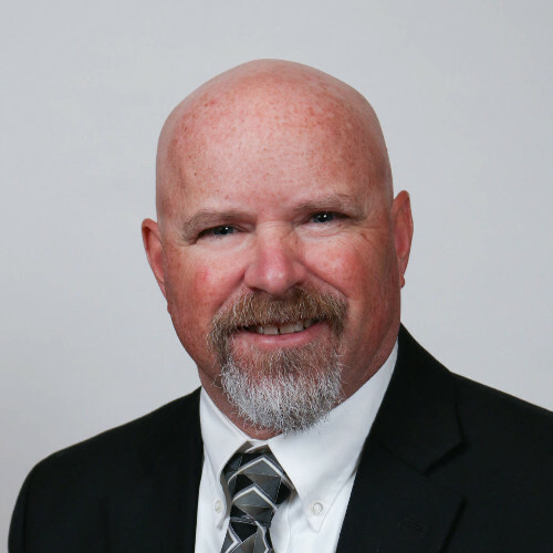 David Lane man with a bald head, beard, wearing a suit and tie against a neutral background.