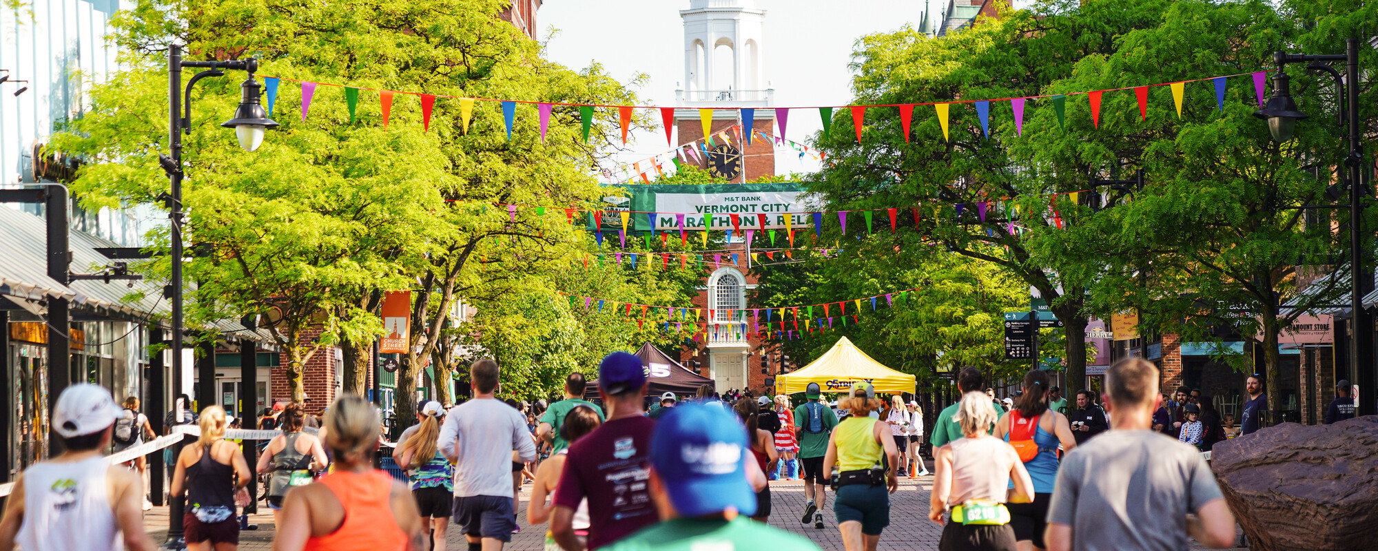 Runners participate in the Vermont City Marathon on a vibrant, decorated street.