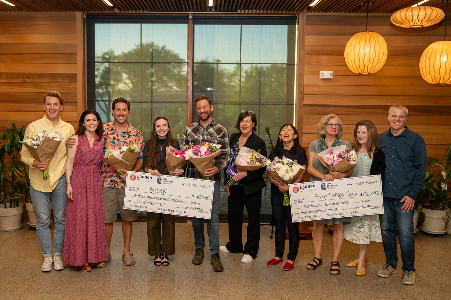 Winners hold checks and bouquets at a celebratory award event.