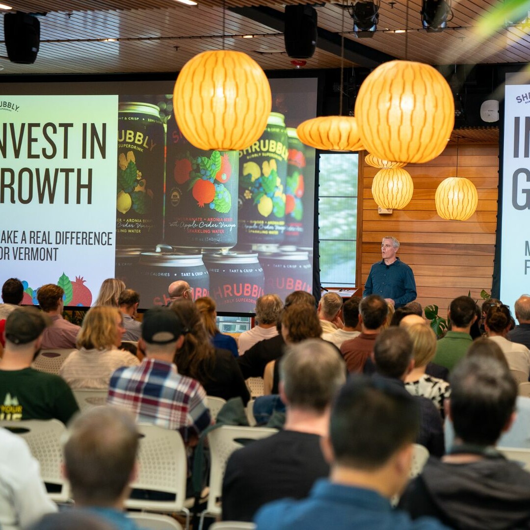 A speaker presents about business growth to an engaged audience, surrounded by stylish decor.