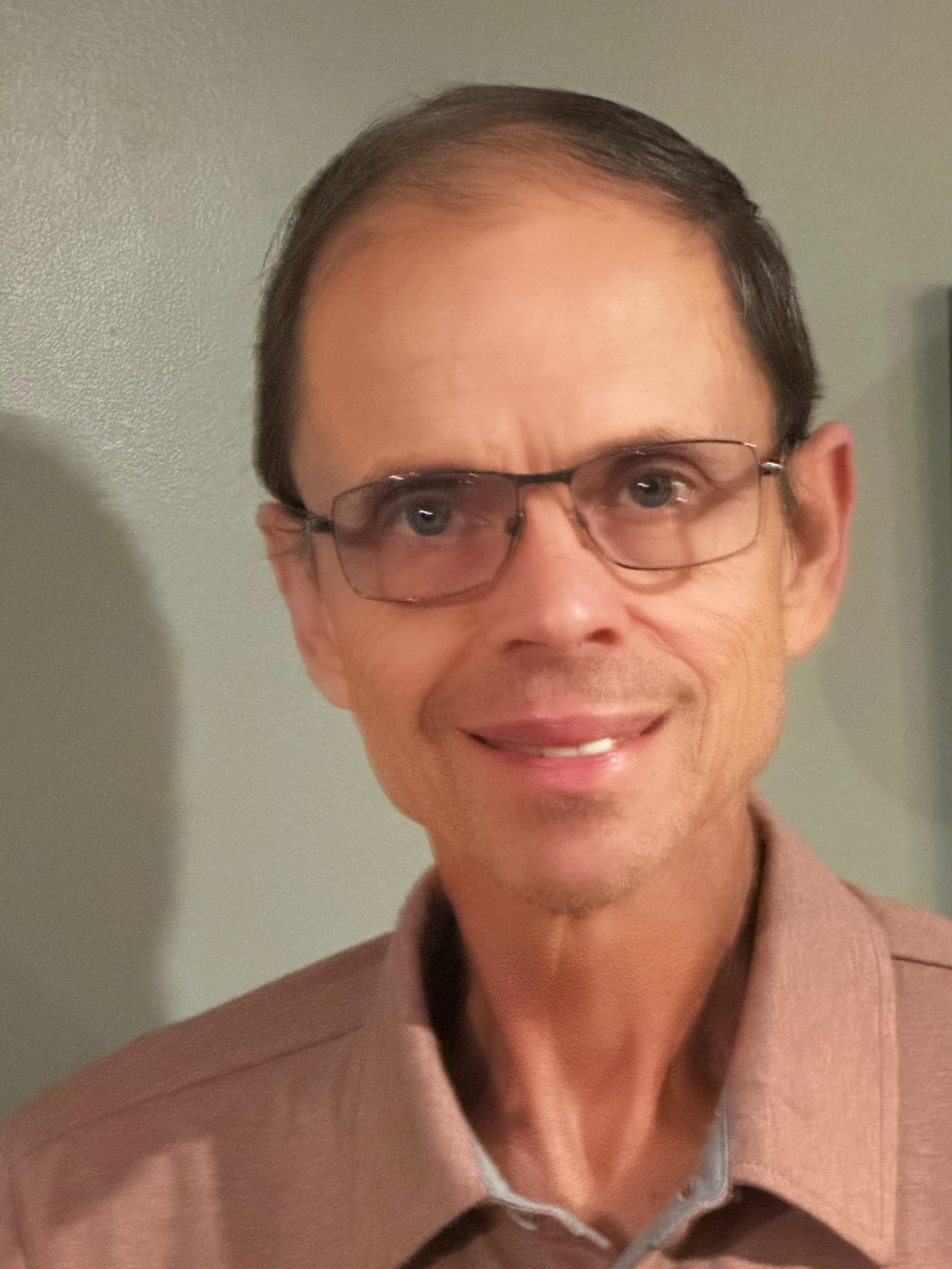 A smiling man with glasses and short hair, wearing a light brown shirt.