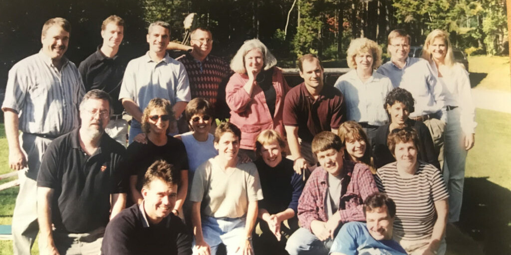 Group photo of 20 people smiling outdoors in a park-like setting.