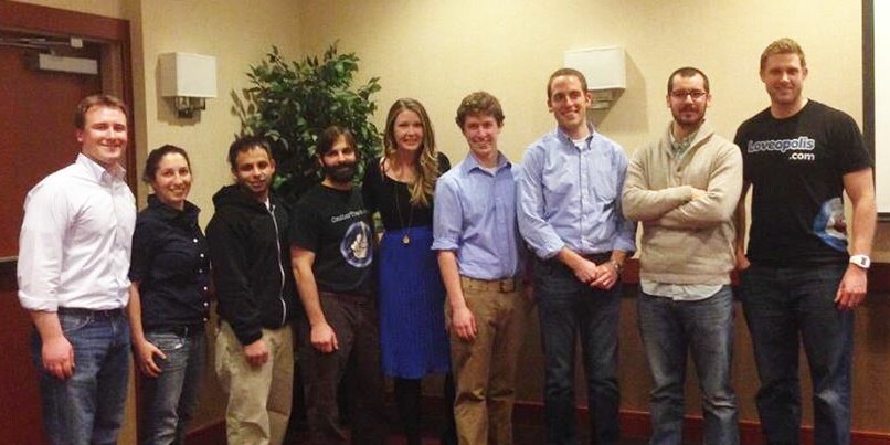 A group of eight people poses together in a casual indoor setting.