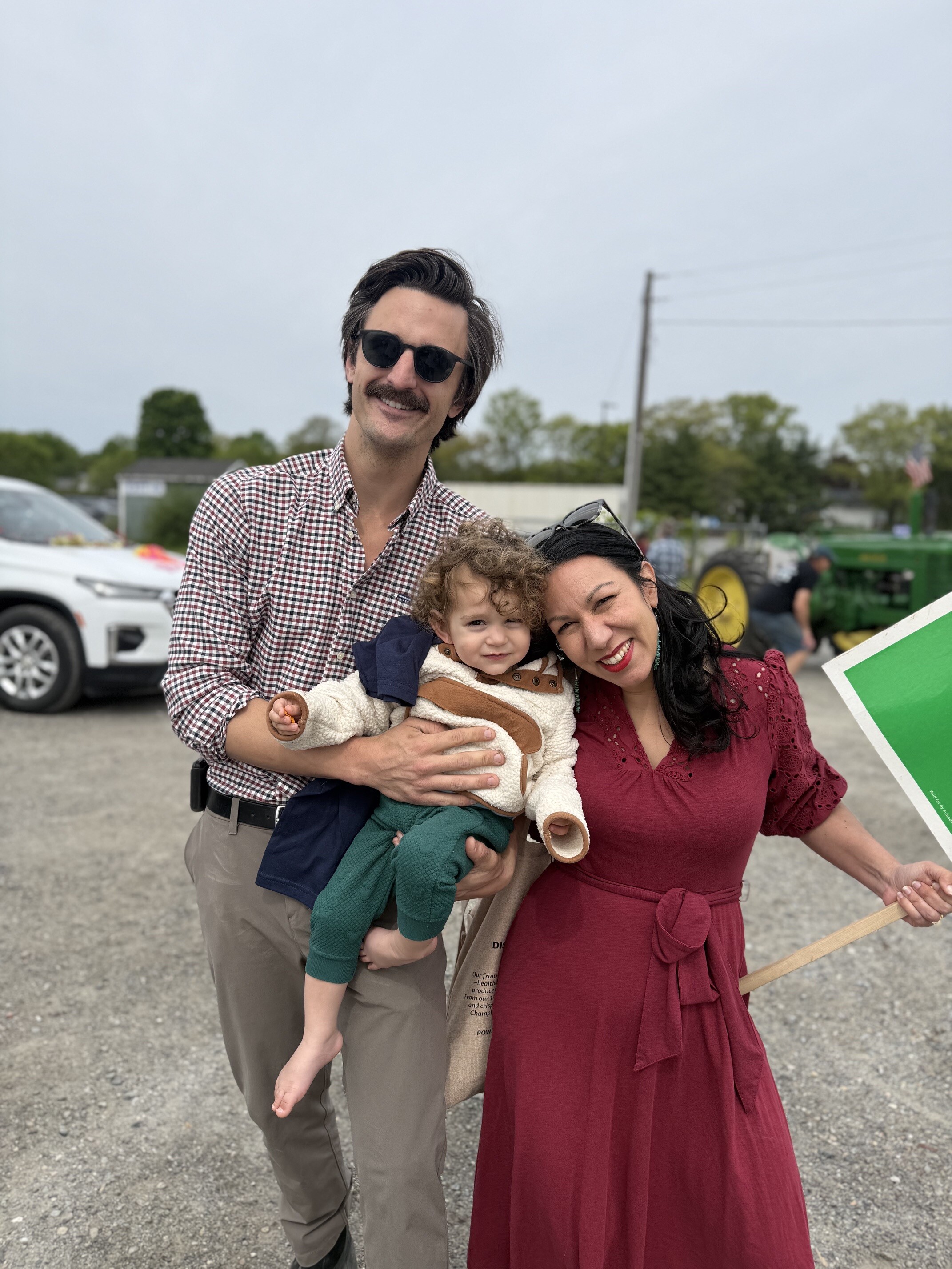 Family portrait featuring a man, woman, and child smiling together outdoors.