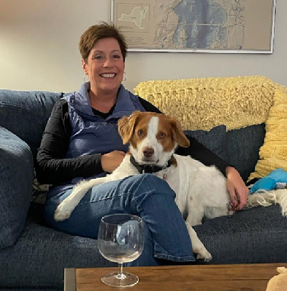 Mari Breen Palace smiling on a couch with her loaner dog, Milo, beside her.