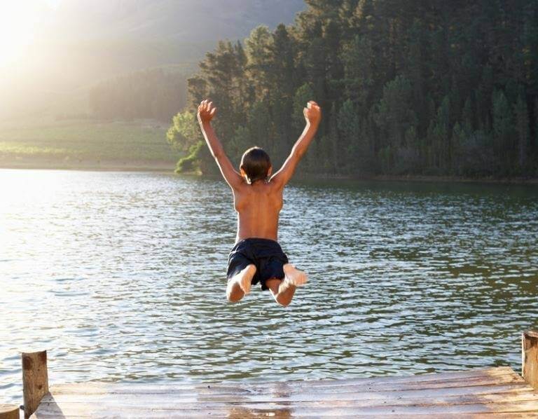 photo of young boy jumping joyfully into a clean lake