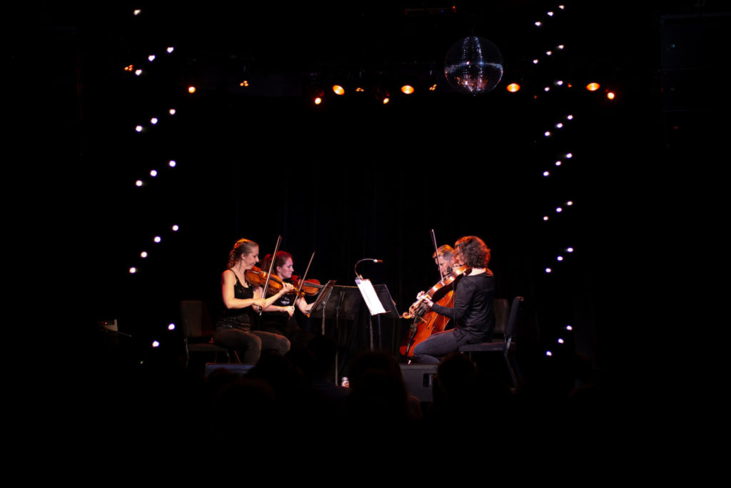 vermont symphony orchestra's string quartet plays on a dark stage surrounded by lights and a disco ball
