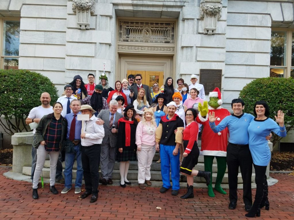 drm law firm staff posing in front of their building wearing halloween costumes and smiling